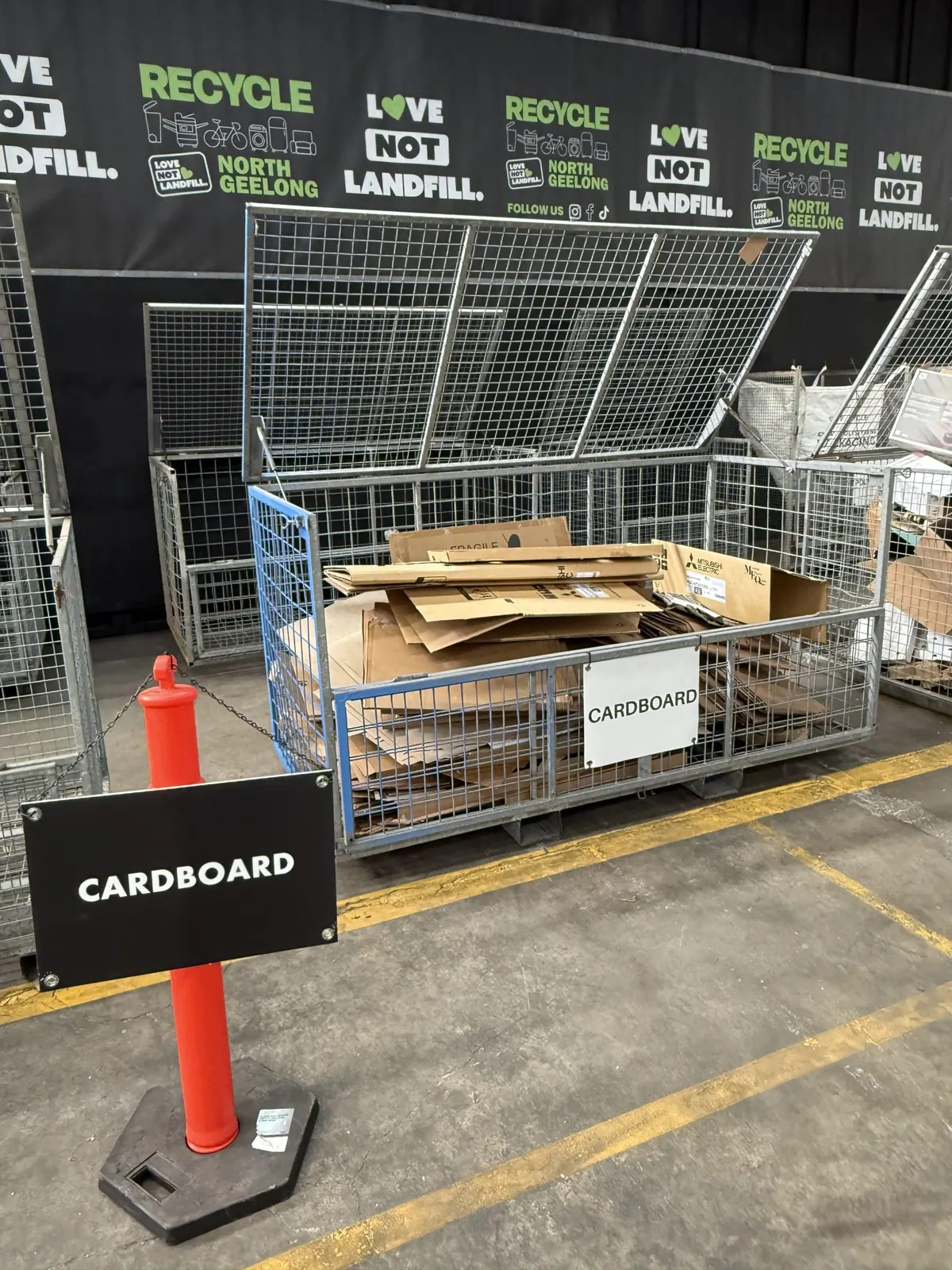Flattened cardboard in a cage under a cardboard sign